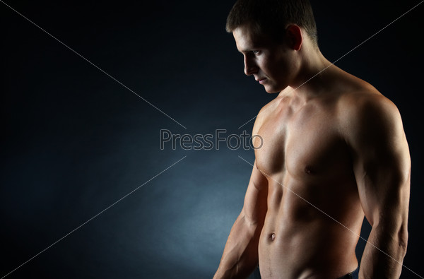 A portrait of a hot guy man without a shirt against dark background with copyspace, stock photo