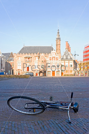 The empty town square, early morning, with an abandoned bicycle and the sun-lit town hall in the background