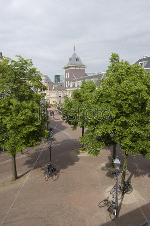 A hotel room view on Haarlem\'s empty streets in the city center, with parked bikes, lush trees, and the new court house in the distance