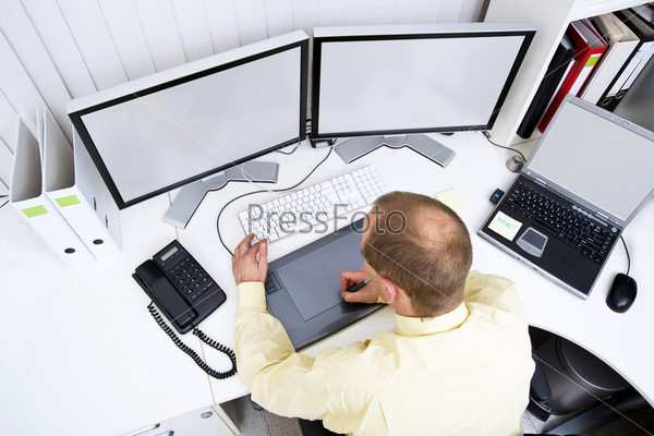Graphic designer at work behind two big flat-screen monitors and a laptop A clipping path of the screens is available at the highest resolution