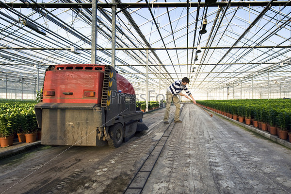 A man sweeping the concrete floor of a huge glasshouse