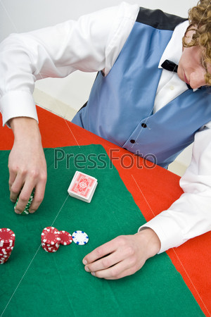 A dealer, counting chips on a poker table, with a deck of cards in front of him.