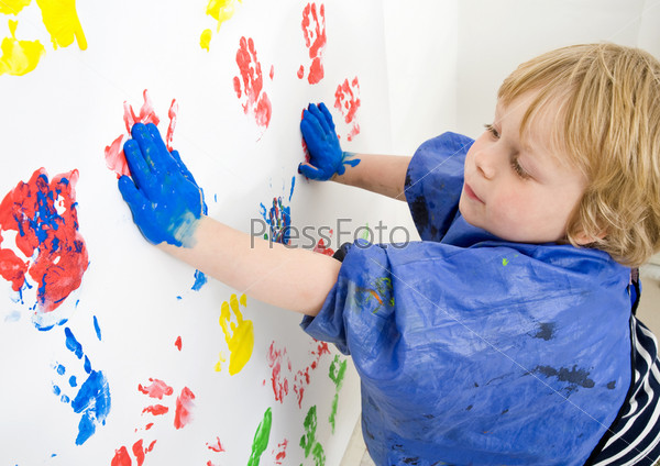 A boy finger painting with blue acrylic paint on a wall