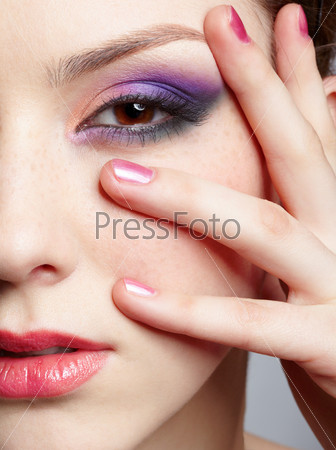 close-up half-face portrait of young beautiful woman with violet eye shadow touching her face with manicured hand