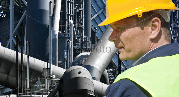 Stern looking worker in front of an imposing factory of a heavy industry facility