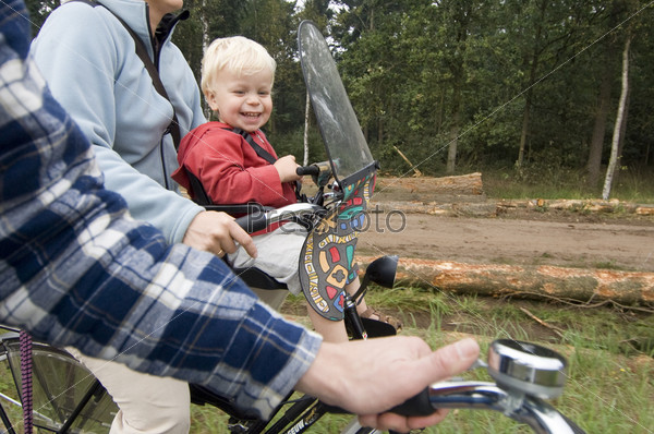 A family on a bike ride, with a little boy in a child\'s\' seat in front of his mother, laughing at his father ringing the bell