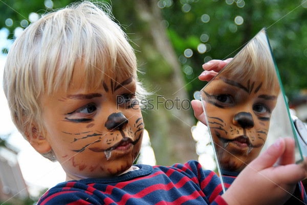 Young boy admiring his painted face in a small mirror