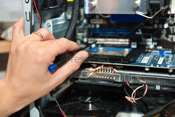 Male hand,  holding a precision screwdriver in front of an open computer. Focus on the fingers holding the screwdriver
