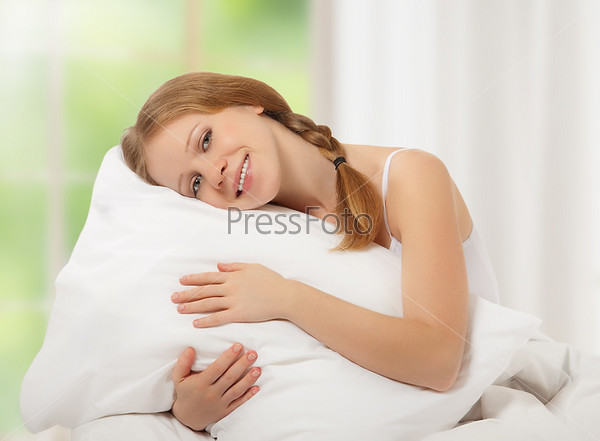happy dreamy beauty girl hugging a pillow while sitting in bed against the window with the green