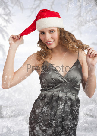 Portrait of a beautiful young Christmas woman wearing Santa hat and evening dress, over winter landscape and snow.