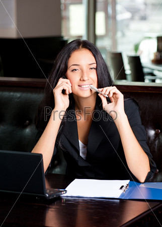 Young attractive business woman working on her laptop and\
talking on the phone in a cafe