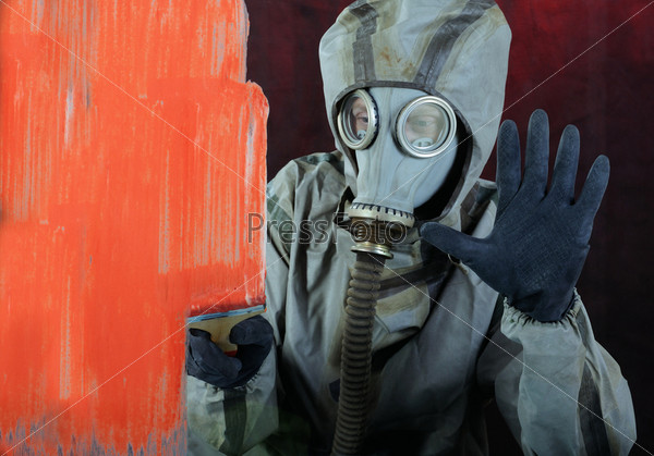 The person in a gas mask paints over glass a red paint