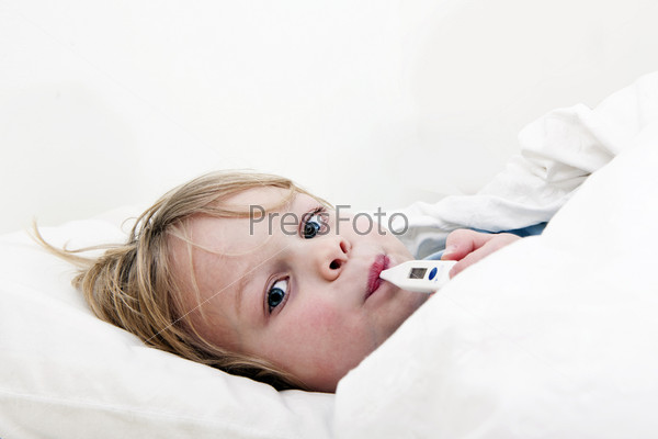 Ill young child, lying in bed with a thermomether, measuring the height of his fever and looking into the camera