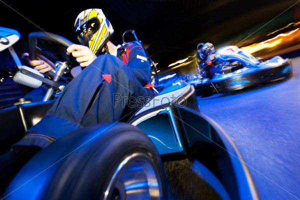 Two go-cart drivers battling in a competitive race on an indoor circuit