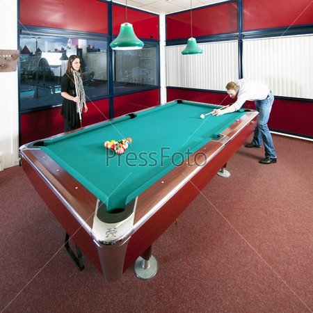 Two people playing pool in a room with a view on an city skyline at dusk