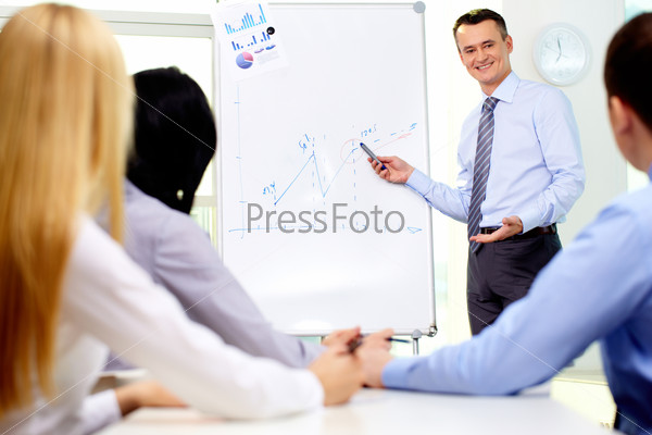 Smiling businessman drawing a graph for his colleagues on the whiteboard