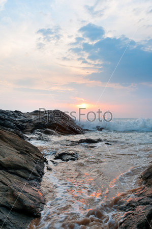 Beautiful stones and waves at sunset under blue sky