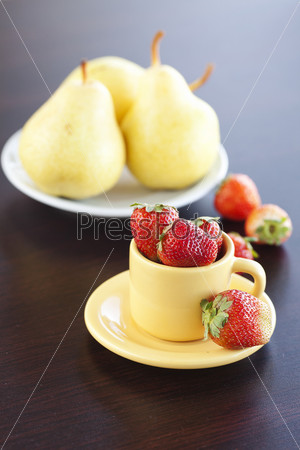 Клубника, груши и чашка с блюдцем на столе