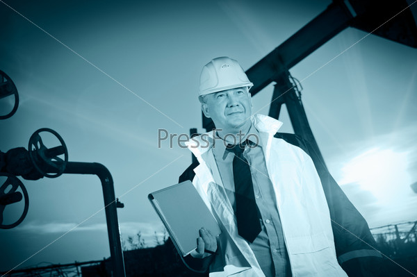 Oil worker in uniform and helmet on of background the pump jack and sunset sky. Toned.