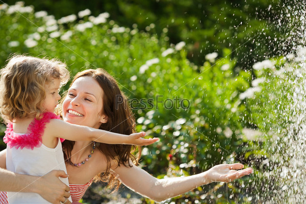Woman with child playing against splashes of water in the summer
