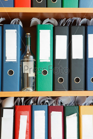 Glass bottle with alcohol hidden between file binders on shelves