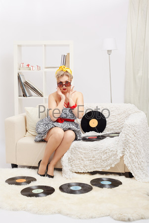 indoor portrait of beautiful surprised young blonde size plus woman model sitting on sofa with vinyl records in interior