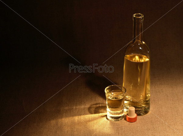 Open bottle of wine or vodka near wineglass on canvas surface under beam of light