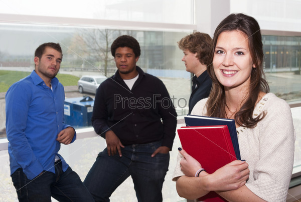 Portrait of a young, female, student, holding a couple of books with a group of guys leaning in the window still in the background