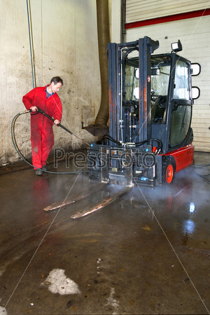 Man cleaning a forklift using a high pressure spray gun with hot, steaming, water in a workshop