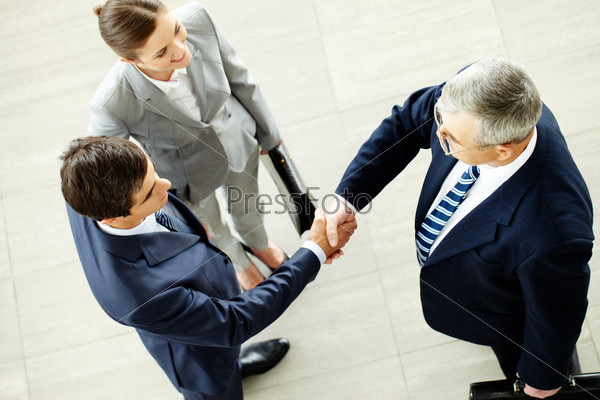 Image of business partners handshaking after striking deal with smart woman near by