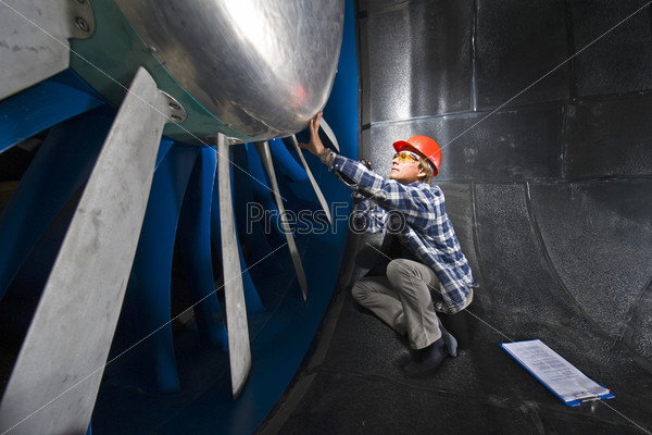 An engineer, wearing the appropriate protective gear, examining the rotor of an industrial wind tunnel facility