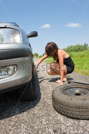 Young woman jacking up her car to change a flat tire with a spare one