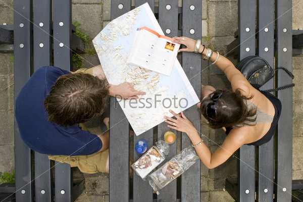 Young couple planning a trip on a map, with a guide book on a pick nick table, with pastries and soda bottles