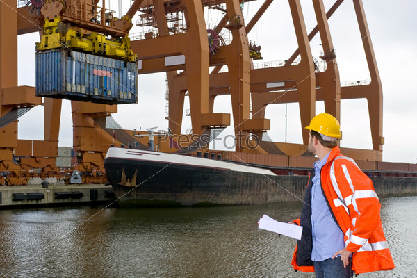 A male customs control officer inspecting the unloading of containers at an industrial harbor