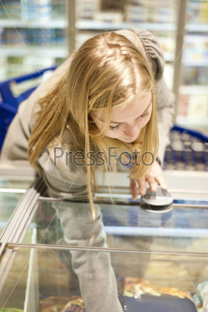 Young woman reaching in a freezer of the frozen food section of a supermarket, shallow Depth of field, focus on the eyelids