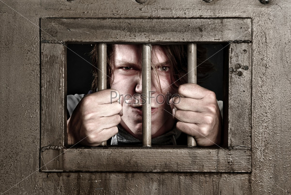 Cross Processed image of a man in prison holding the bars of his cell door.