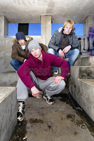 Three angry looking gang members in a dirty, concrete bunker at dusk.