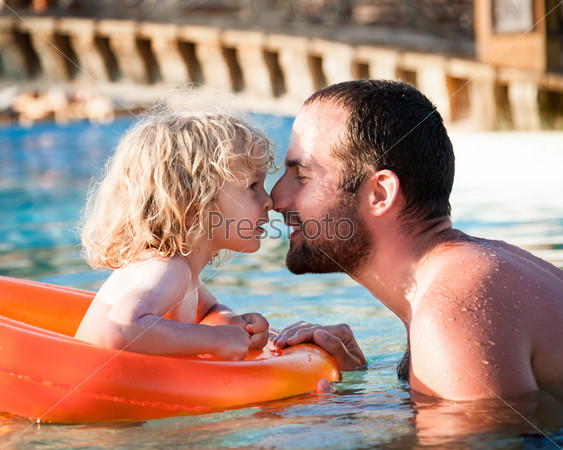 Happy child playing with father in blue water of swimming pool on a tropical resort at the sea Summer vacations concept