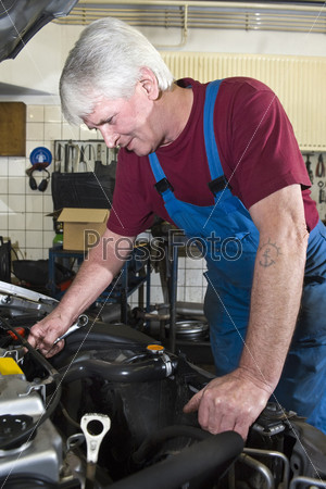 A senior motor mechanic servicing a car inside a garage