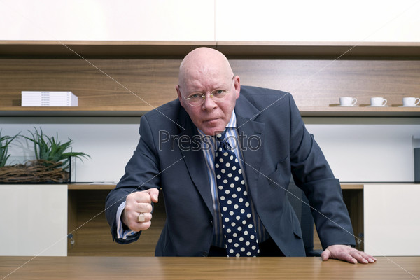 An angry senior manager slamming his fist on the desk in front of him.