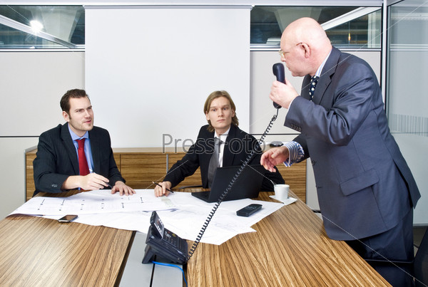 A business meeting with two young associates and a senior manager discussing plans and talking to a client on the phone