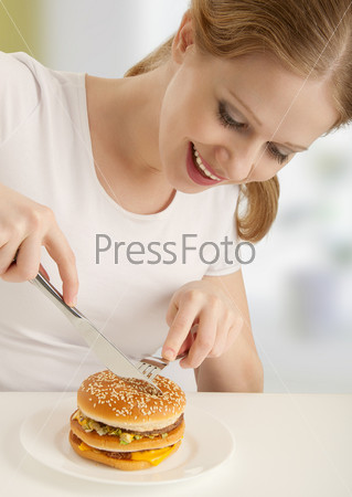 Attractive girl with a fork and knife eats hamburger