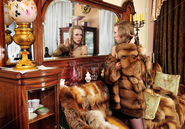 Woman in fur coat at the mirror in Luxurious classical interior.