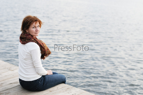 Middle age woman sitting on wood boards by the water, stock photo