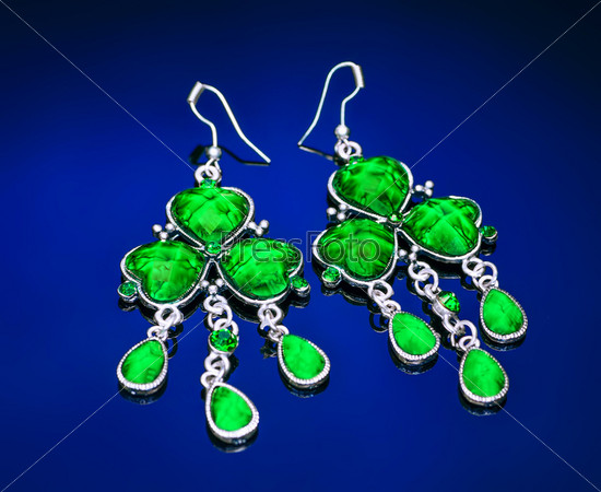 Earrings with green gemstone on a blue background