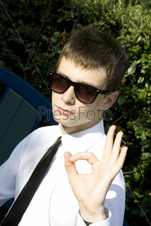 Teenager in a park sitting on a bench in a white shirt and tie, looking away. Sign OK