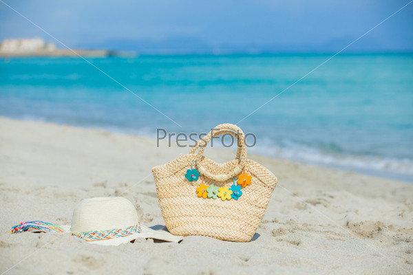 Photo of straw beach hat and bag with flowers on exotic white sand beach
