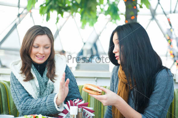 Two beautiful women drinking coffee, having lunch and chatting at cafe