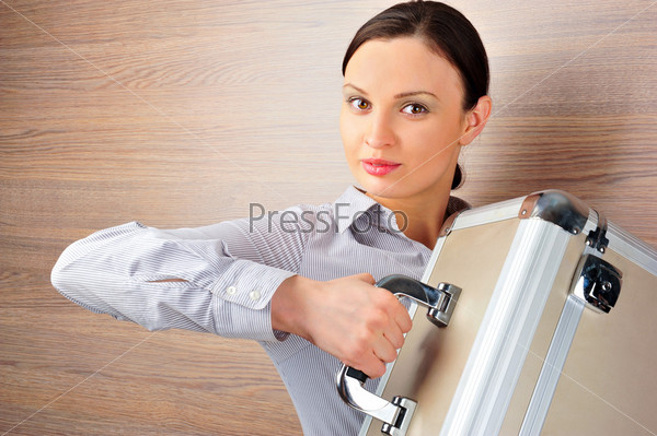 Portrait of emotional pretty young woman against modern stylish wooden wall holding big metal case