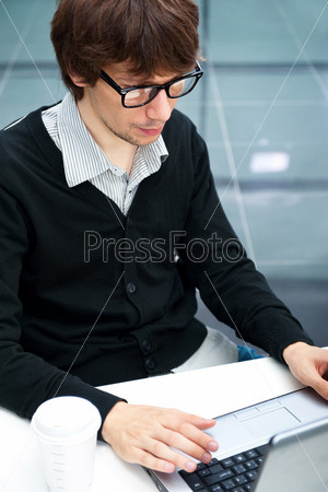 Friendly executive sitting in front of laptop in his office. Big window at the background. Looking away, daydreaming